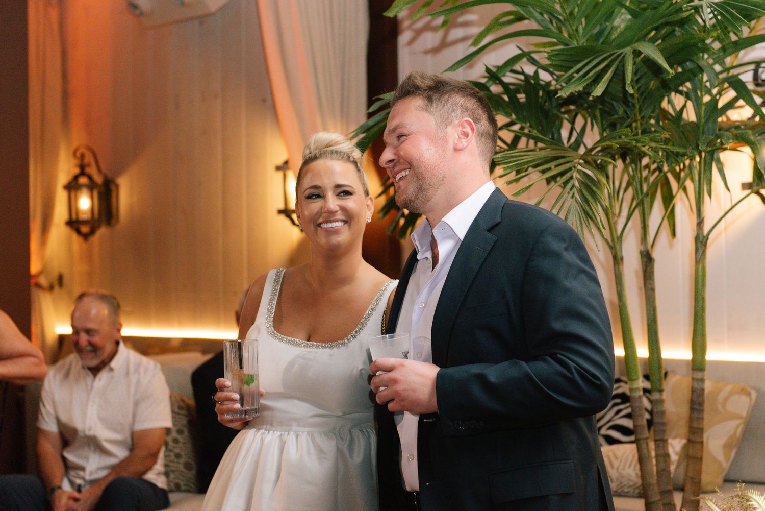 Guests mingling at an elegant indoor reception with tropical palm decorations.