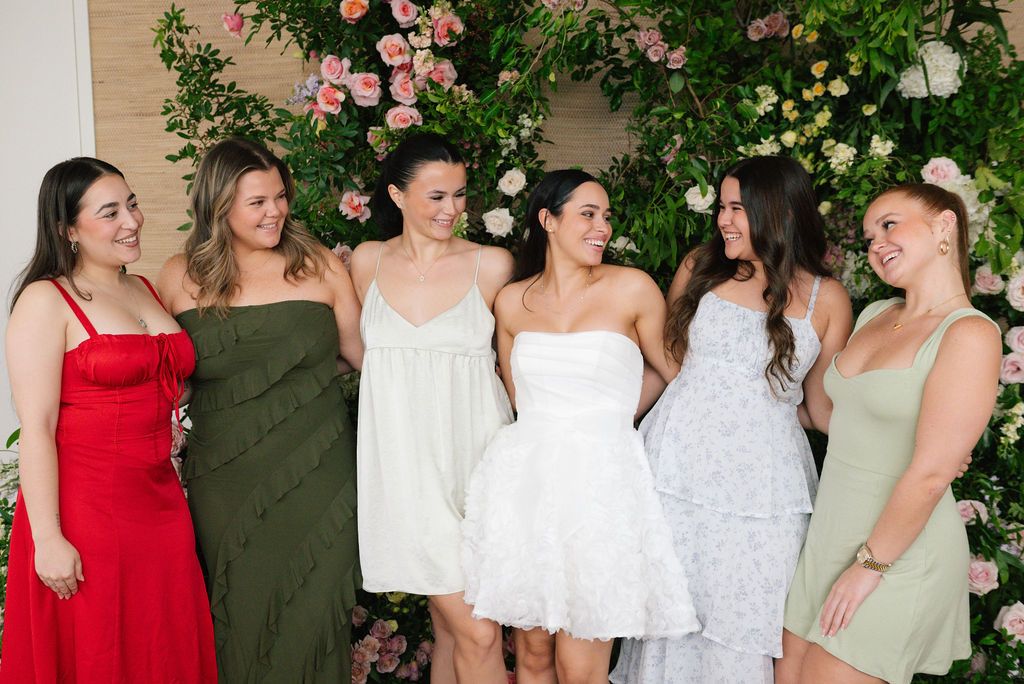 Group photo of bridesmaids in pastel dresses standing together at an elegant garden party.