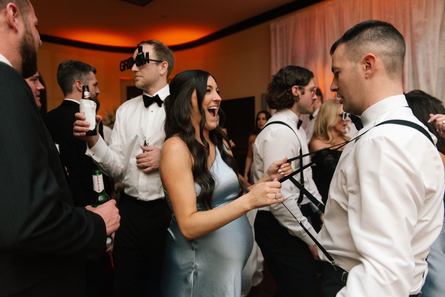 Guests in formal attire dance and celebrate at an elegant wedding reception with warm lighting.