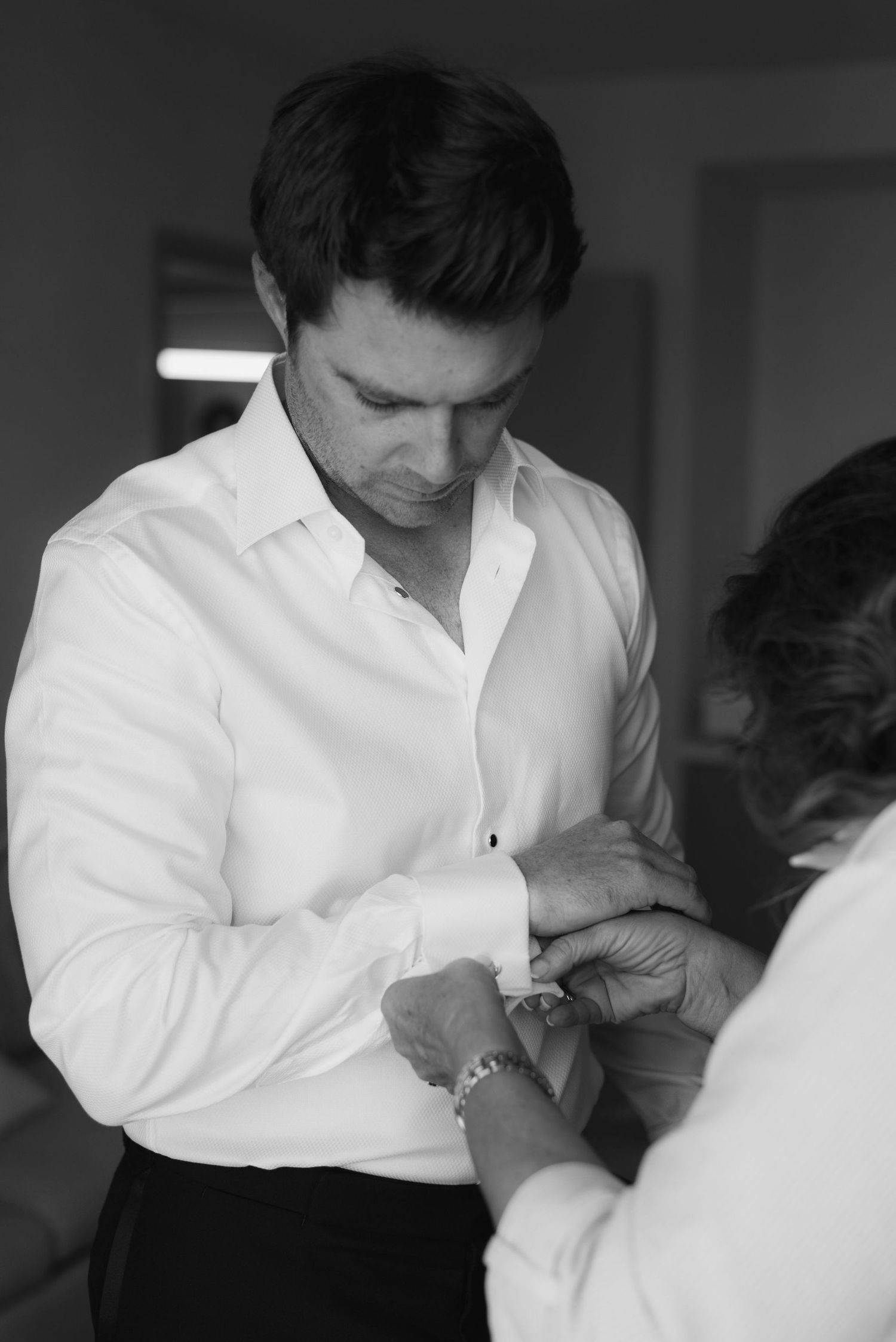 Black and white photo showing someone in a white dress shirt getting help with their cufflinks before a formal event.