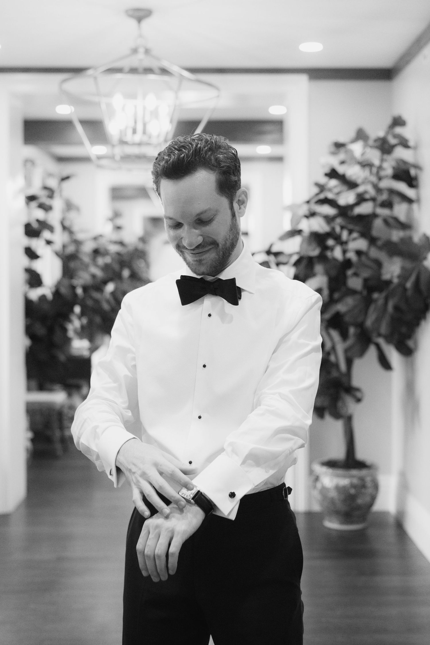 Groom in white tuxedo jacket and black bow tie adjusts his cuffs.