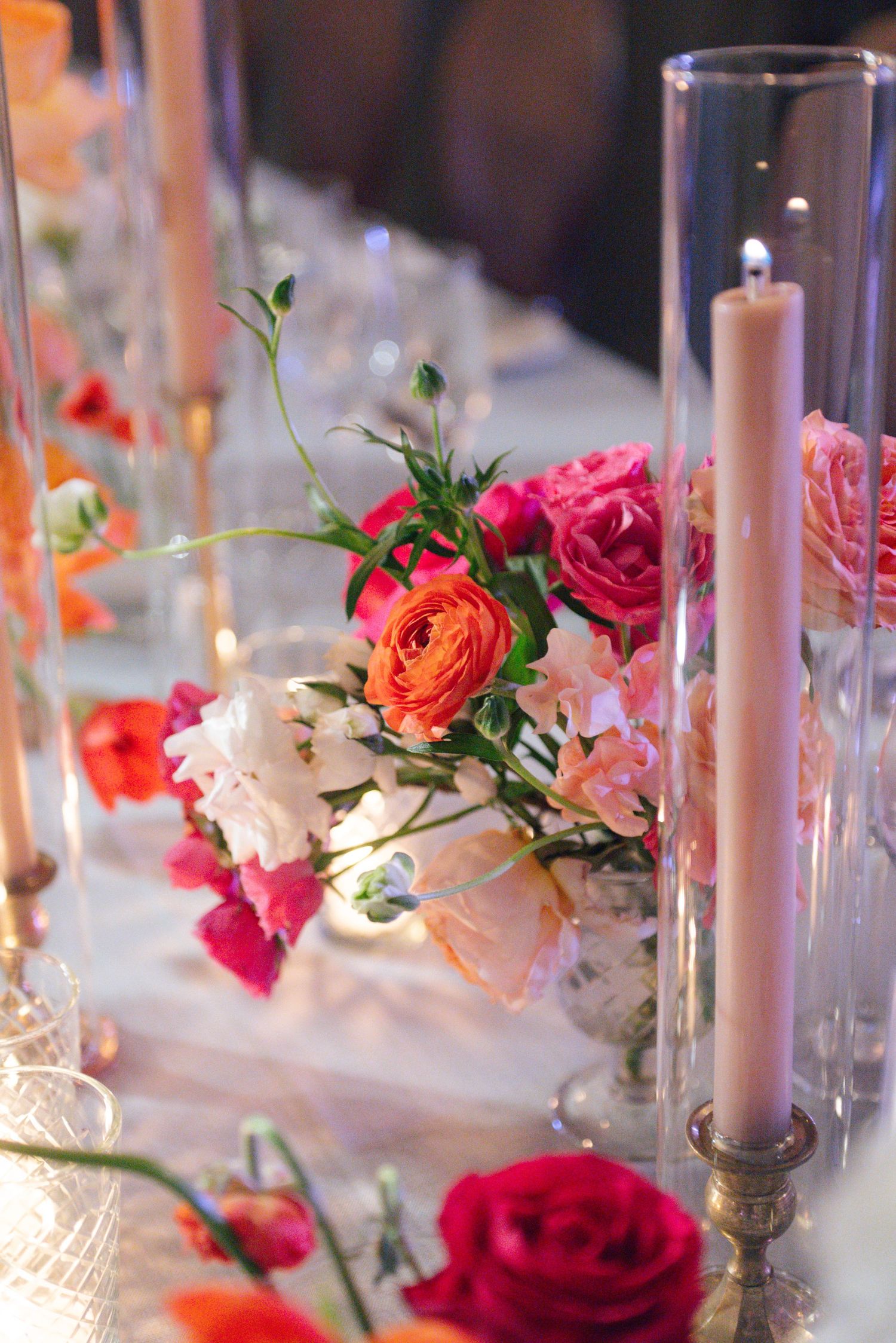 Elegant wedding table setting with pink and coral roses, white candles, and glass centerpieces.