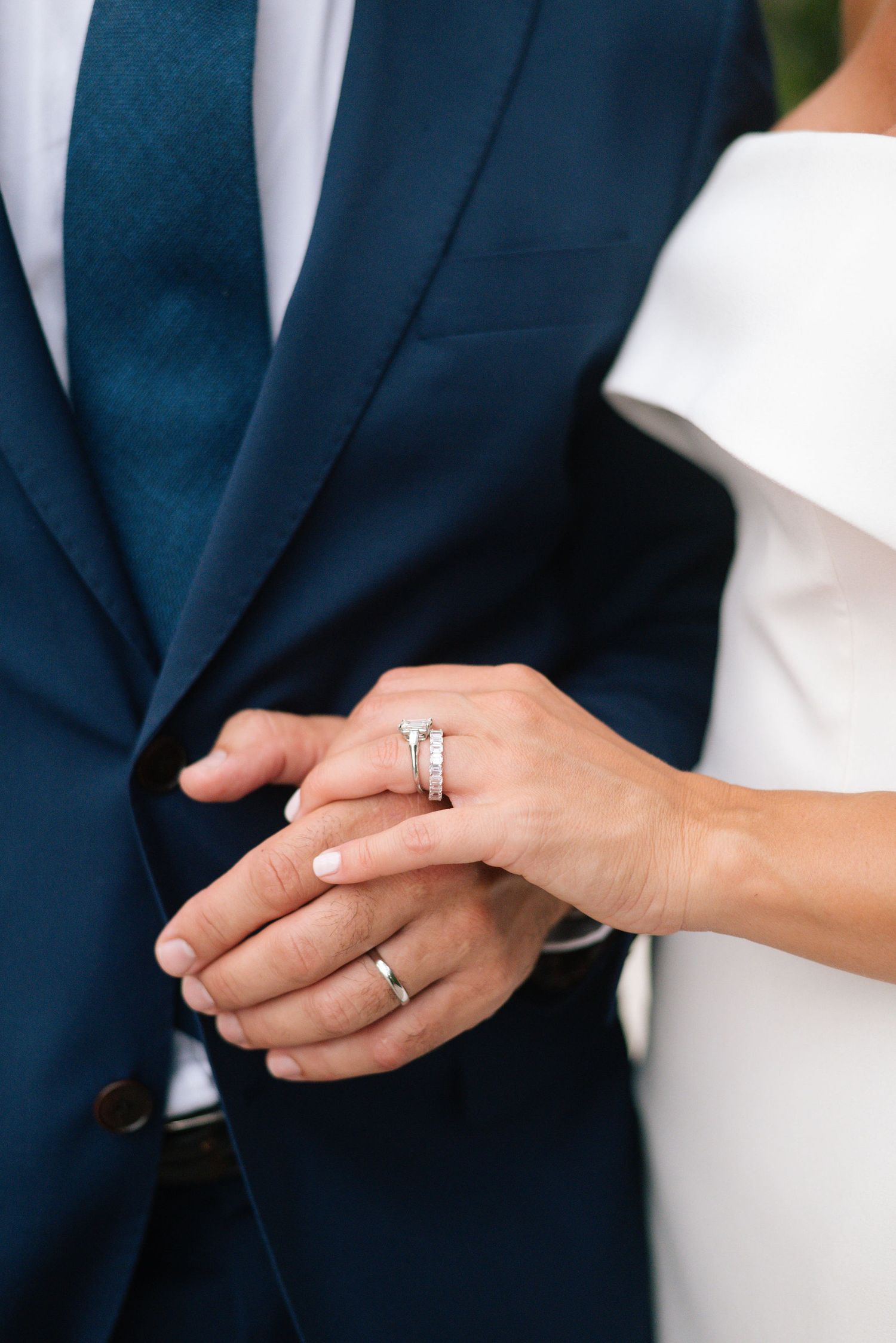 Close-up shots of hands with wedding rings against navy suit backdrop.