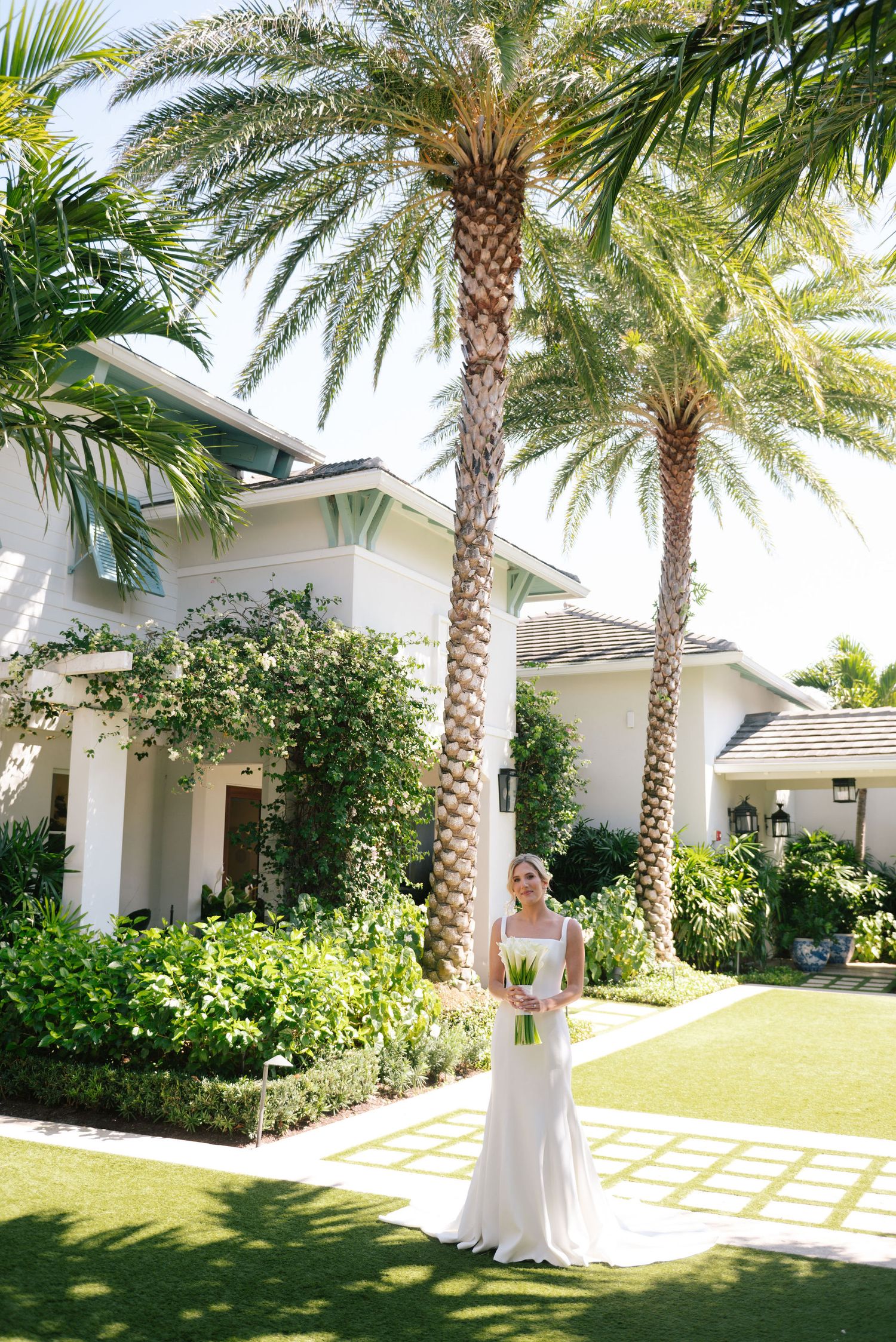 Elegant bridal portrait in tropical garden setting with palm trees and white architecture.