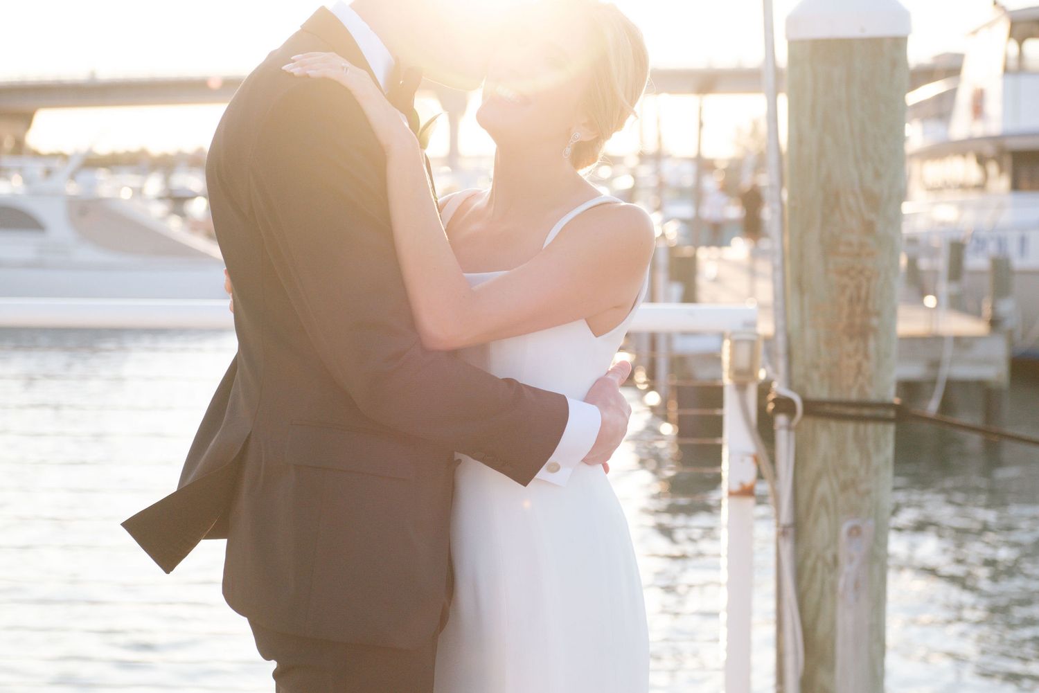 Romantic waterfront wedding photos with marina and boats in the background at sunset.