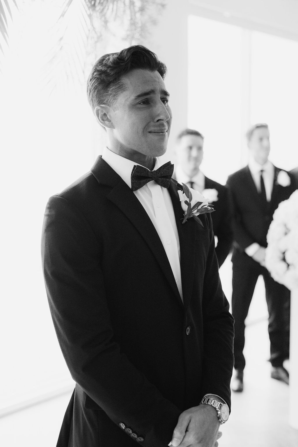 Black and white photo of groomsmen sharing an emotional moment during wedding ceremony.