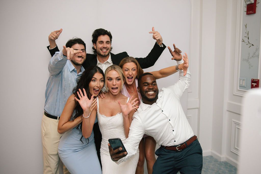 A joyful group celebrates at a wedding reception with raised arms and excited expressions.