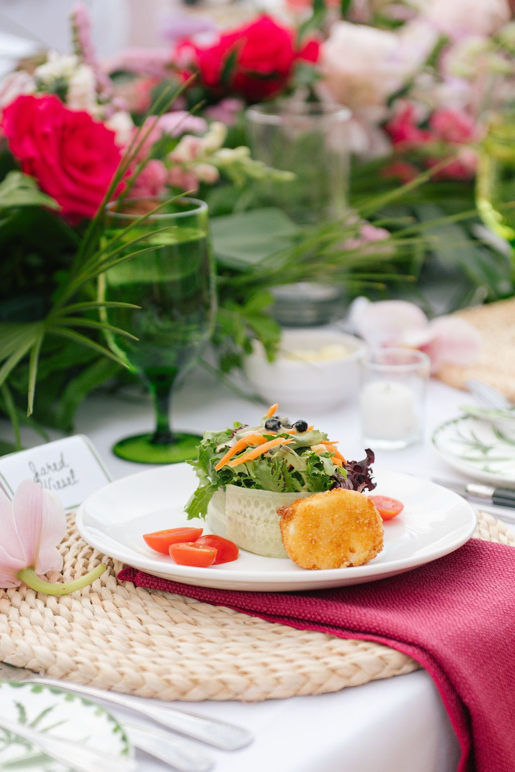 Close-up of gourmet plated dishes on white plates with floral decorations at an upscale event.