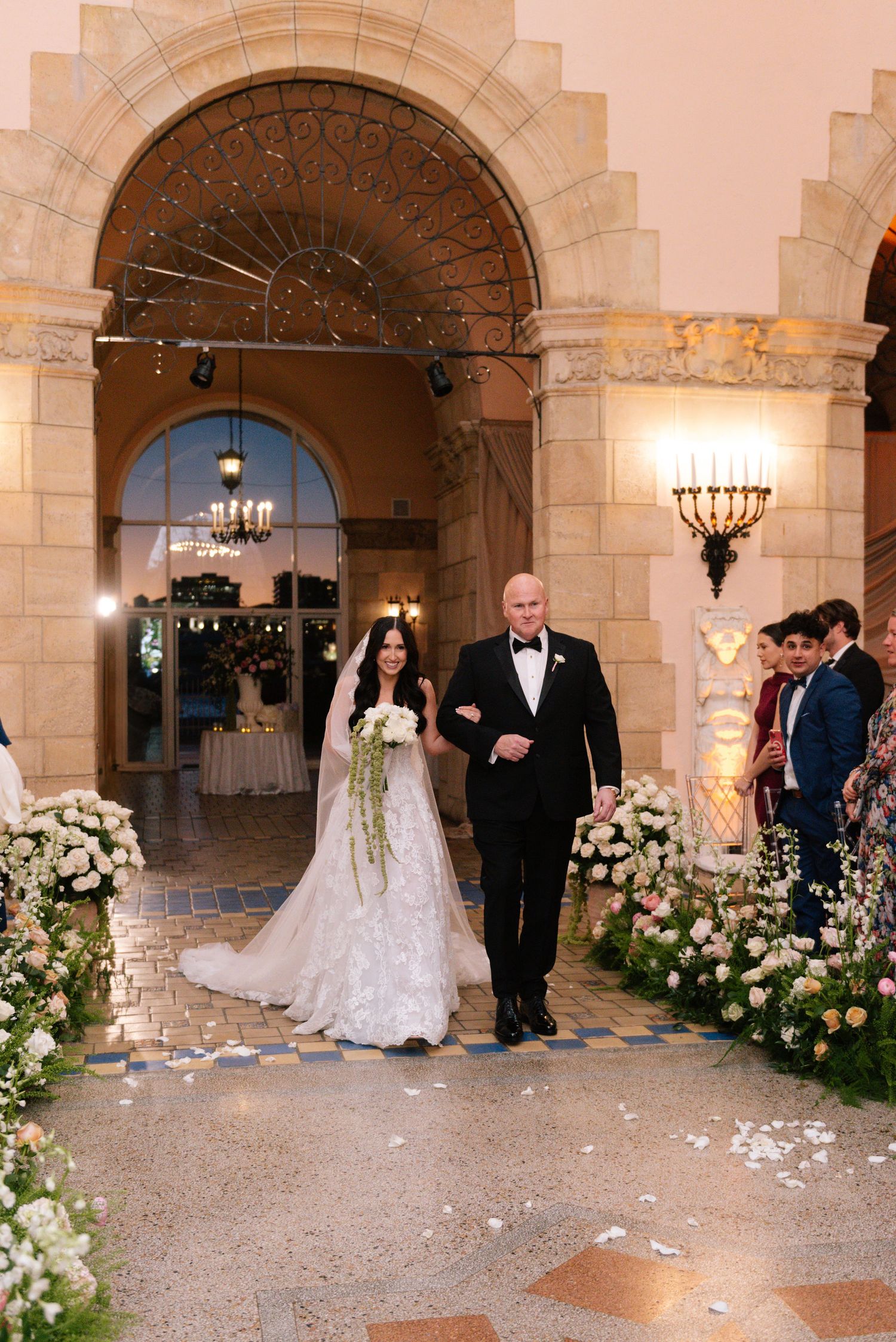Wedding ceremony setup in a grand stone archway with floral decorations and scattered petals.