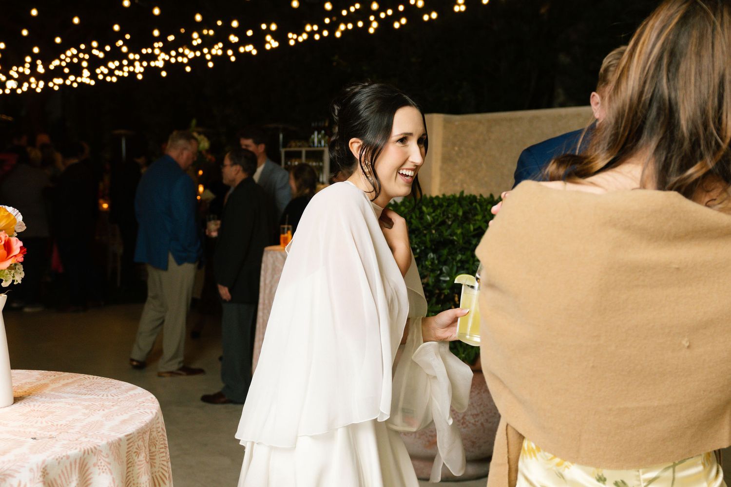 An elegant evening wedding reception with string lights and guests mingling outdoors.