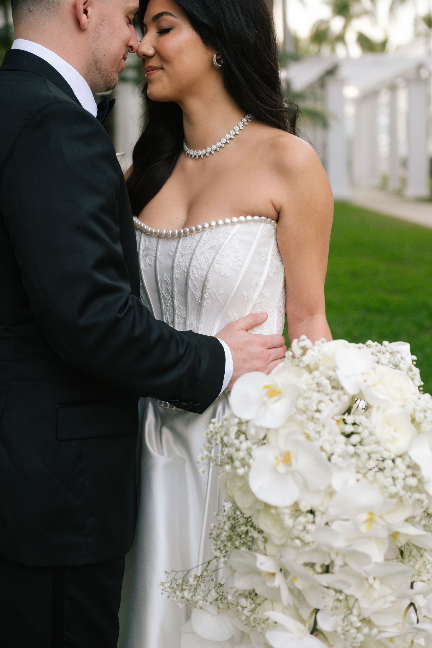 Intimate wedding portrait with a stunning white orchid bouquet and diamond necklace details.