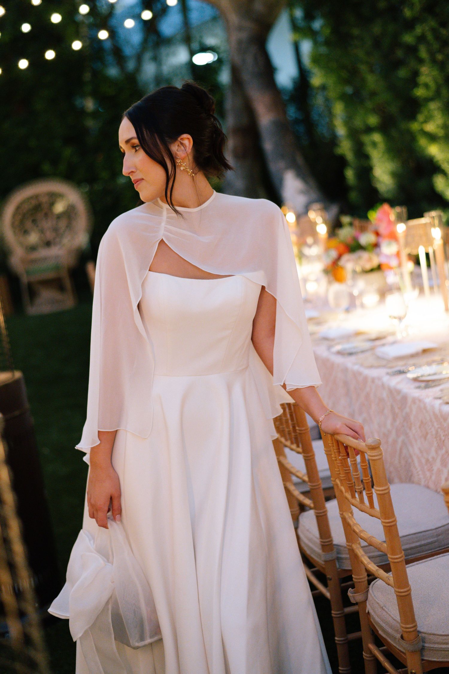 Elegant white flowing dress detail against garden party setting with string lights.