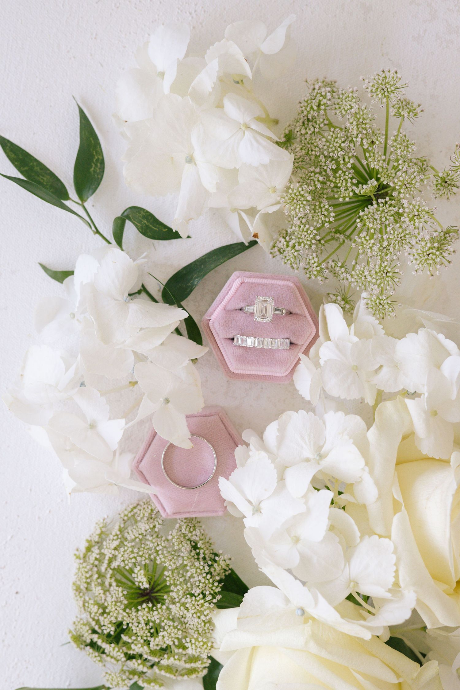 White floral arrangement with roses and baby's breath surrounding a pink hexagonal ring box.