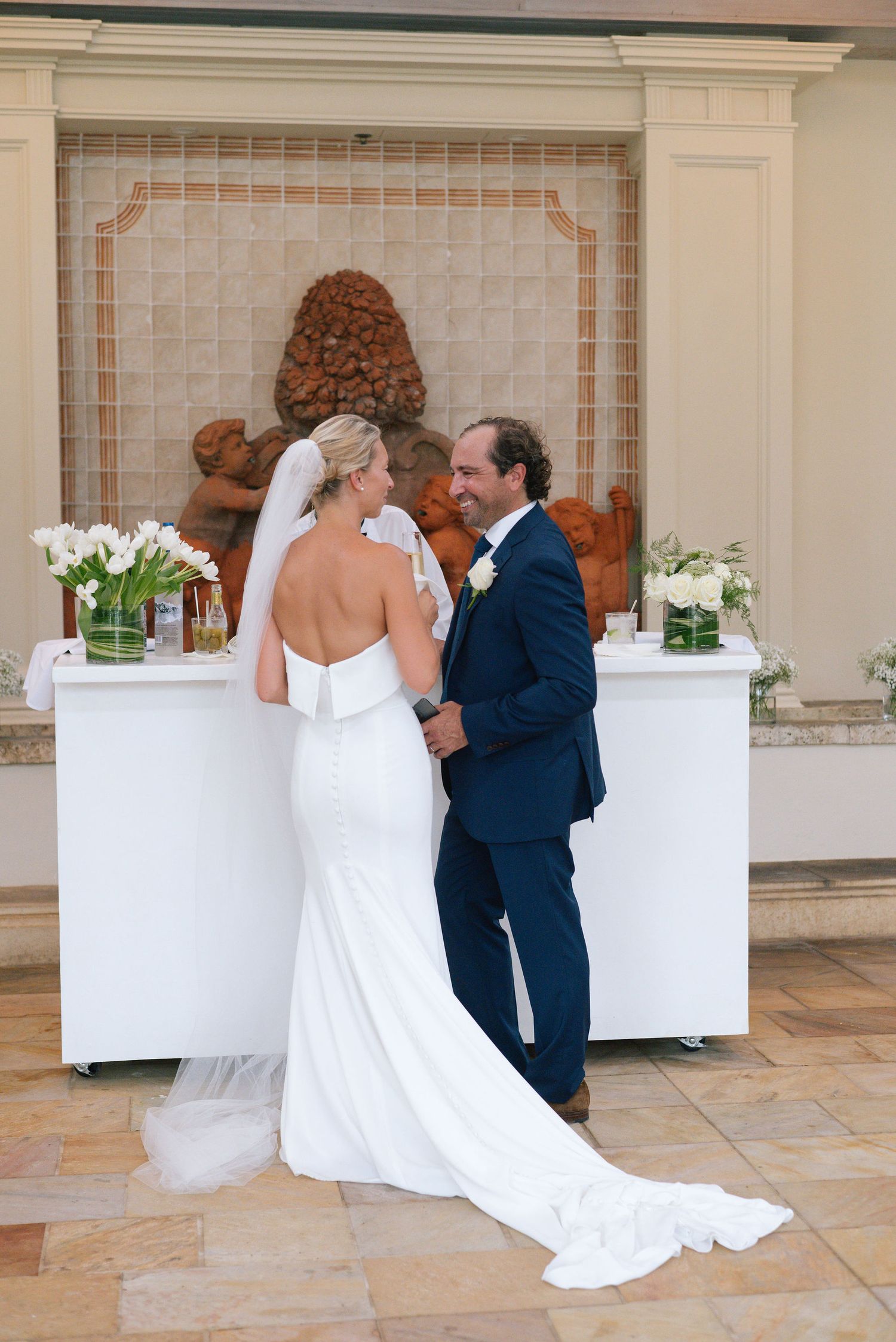 Wedding celebration in an elegant indoor venue with white decor and tiled floors.