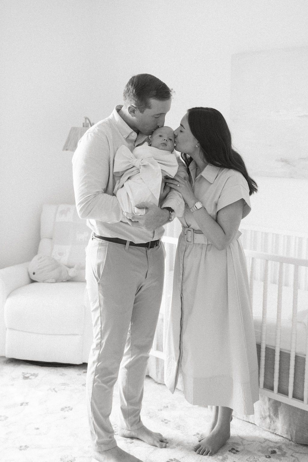 Family poses together in a bright white nursery room with a crib.