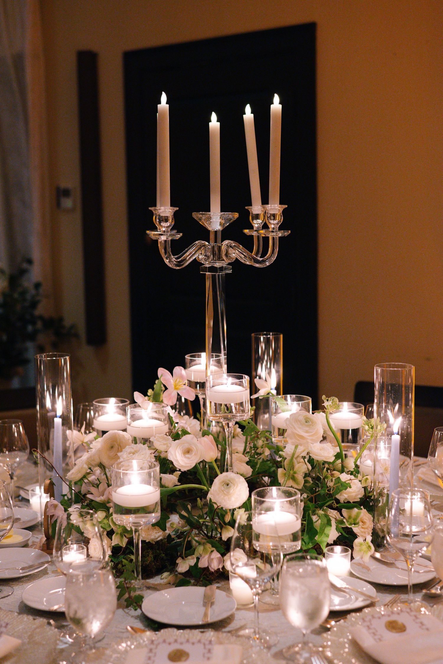 Elegant wedding table centerpiece with silver candelabra, white floral arrangements and glowing votives on a formal dining table.