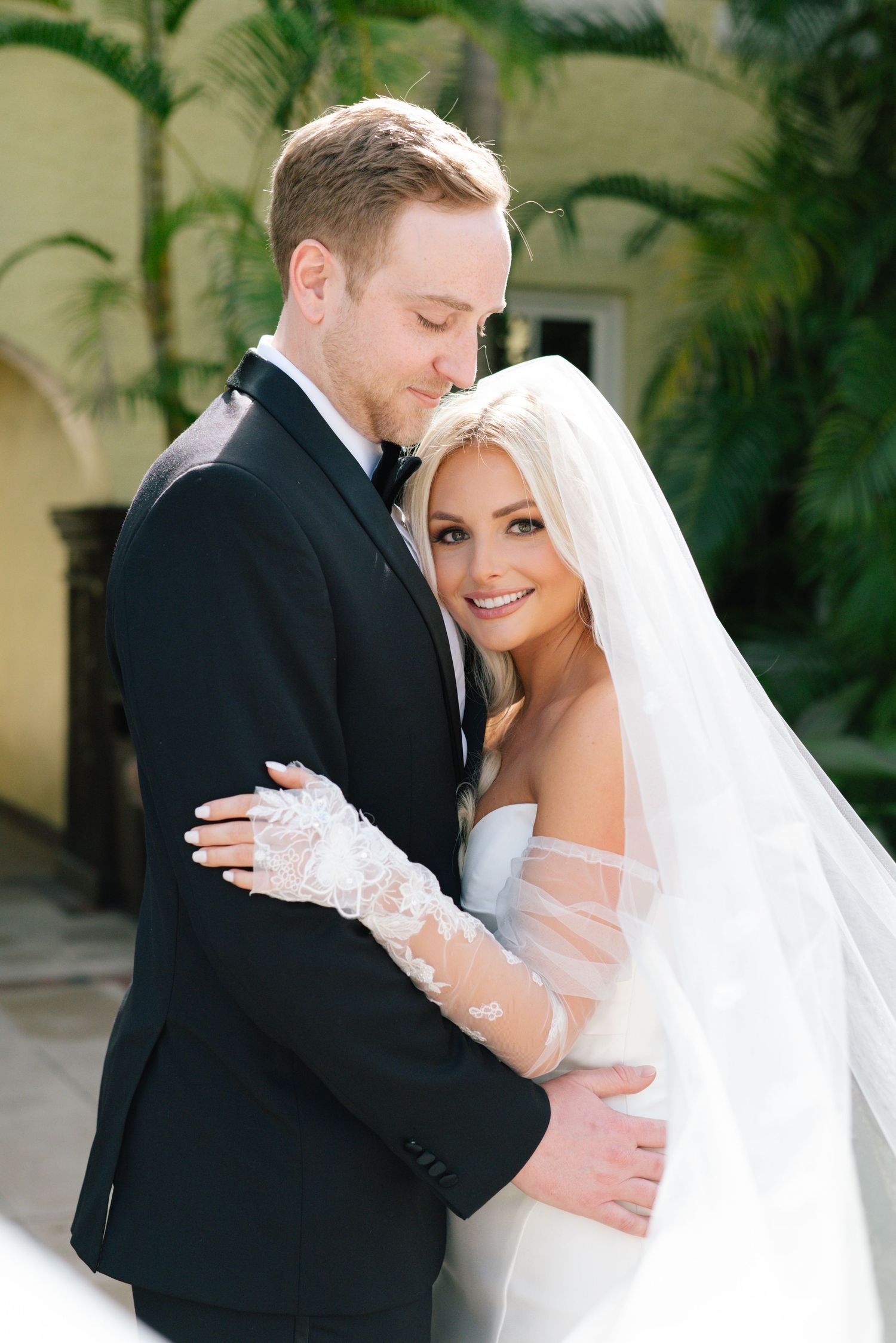 Newlyweds share intimate embrace during wedding photoshoot in garden setting.