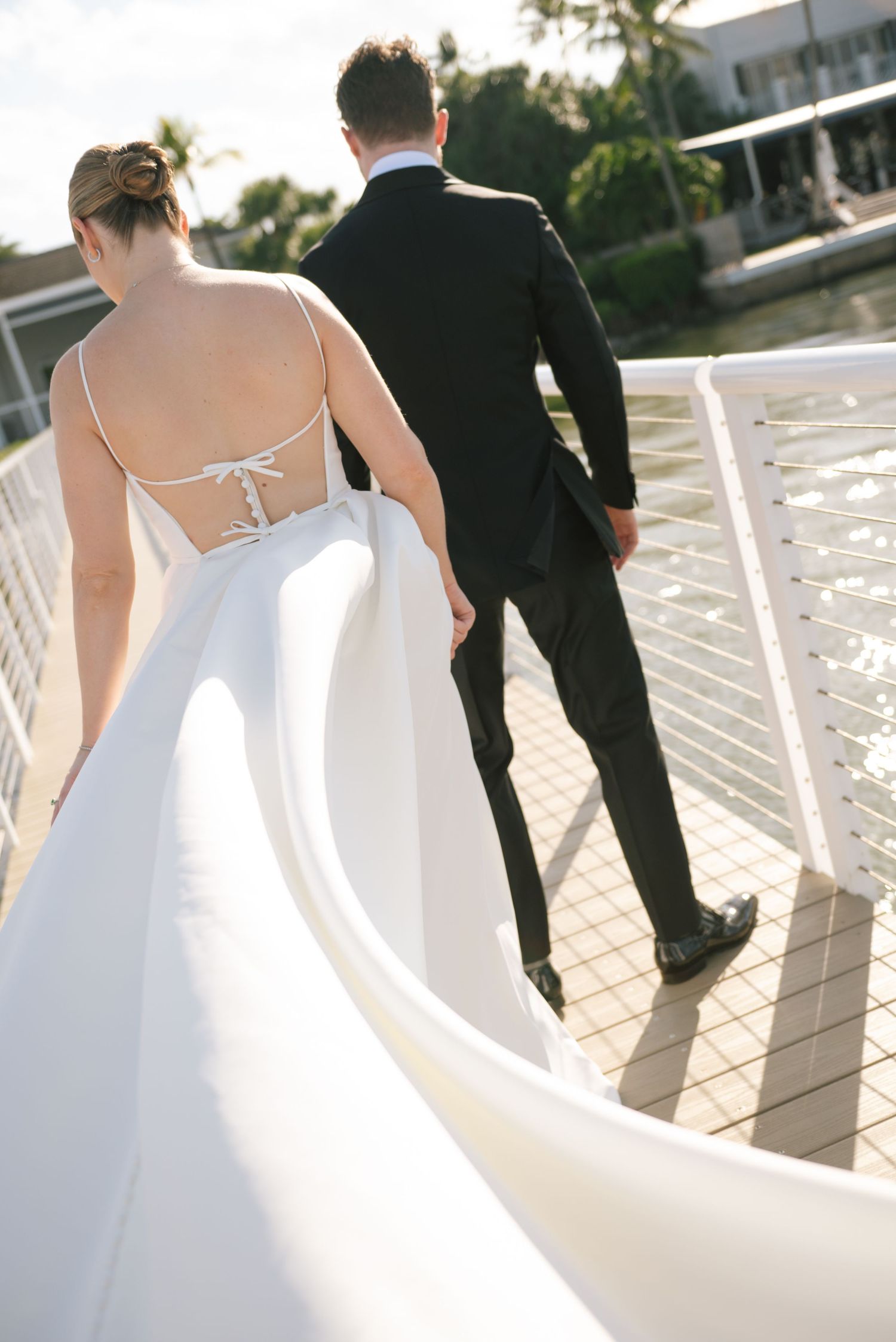 Newlyweds walking along waterfront deck in elegant wedding attire.