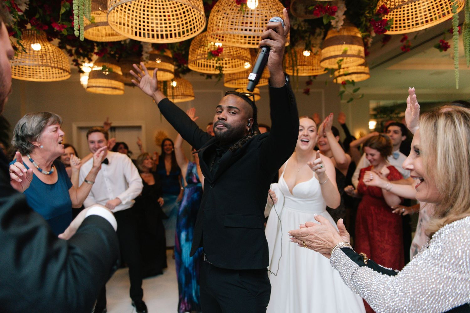 Wedding reception dance floor filled with guests celebrating under warm rattan pendant lights.