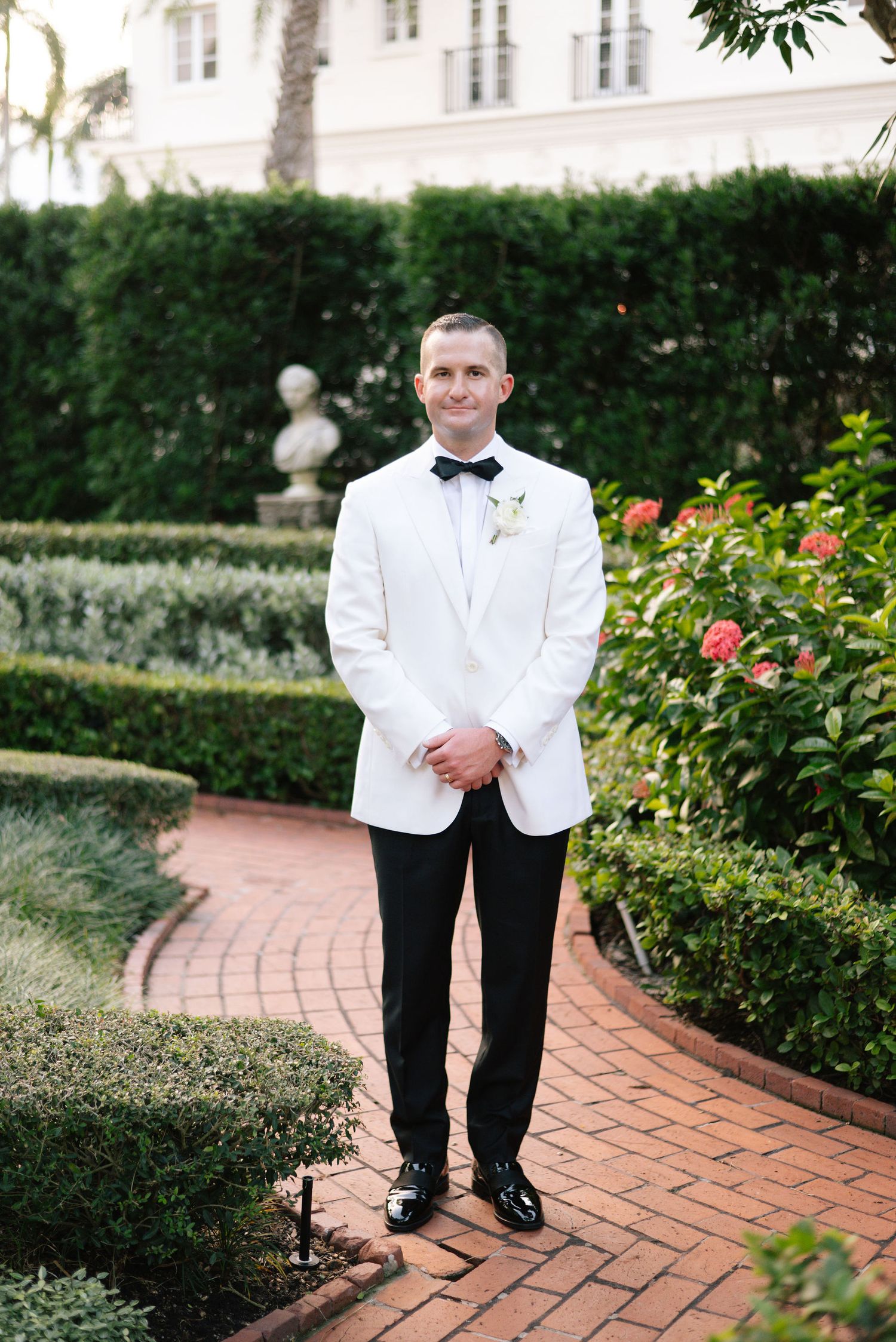 White formal shoes on brick pathway surrounded by manicured garden hedges and flowers.