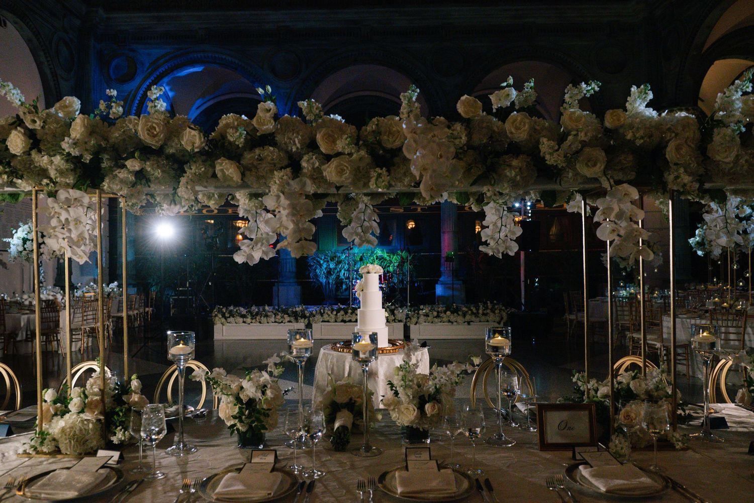 Luxurious wedding tablescape with towering white floral arrangements and gold accents in a grand ballroom.