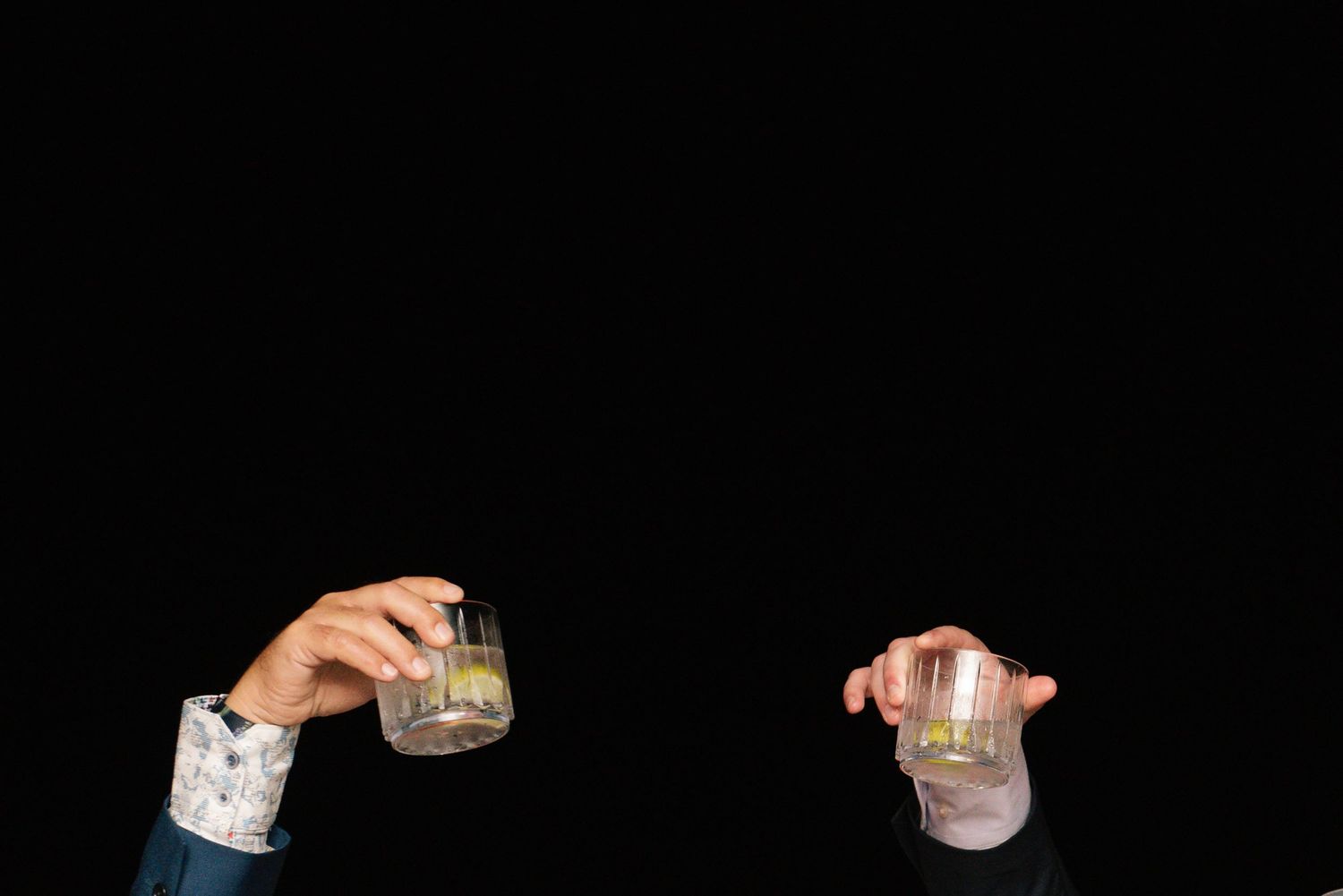 Hands holding cocktail glasses in a dark setting during a social gathering.