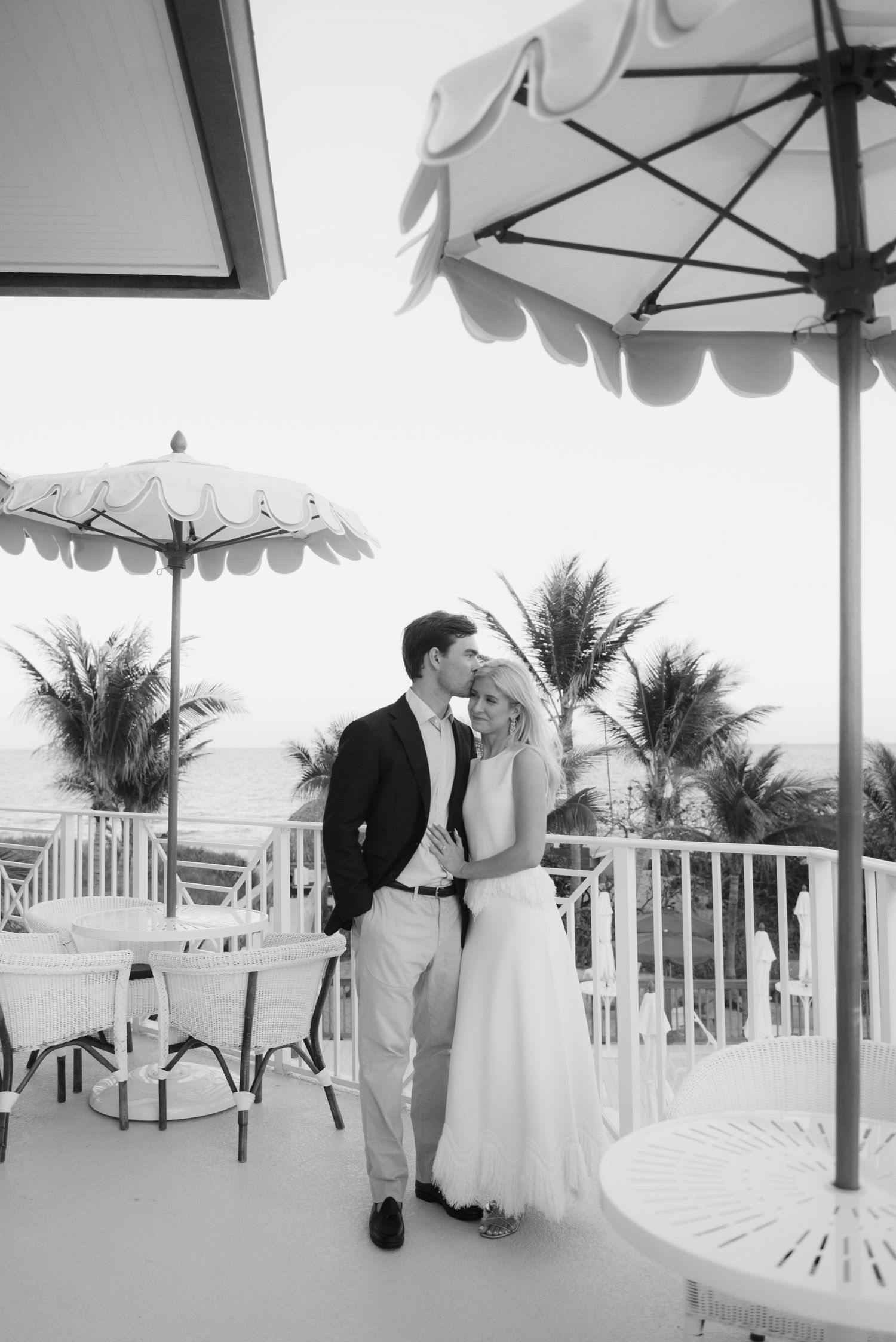 Black and white photo of a romantic moment on a palm-fringed balcony under decorative umbrellas.