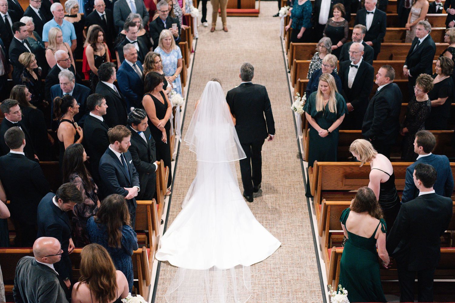 A wedding ceremony in a church with guests seated in wooden pews watching the bride walk down the aisle.
