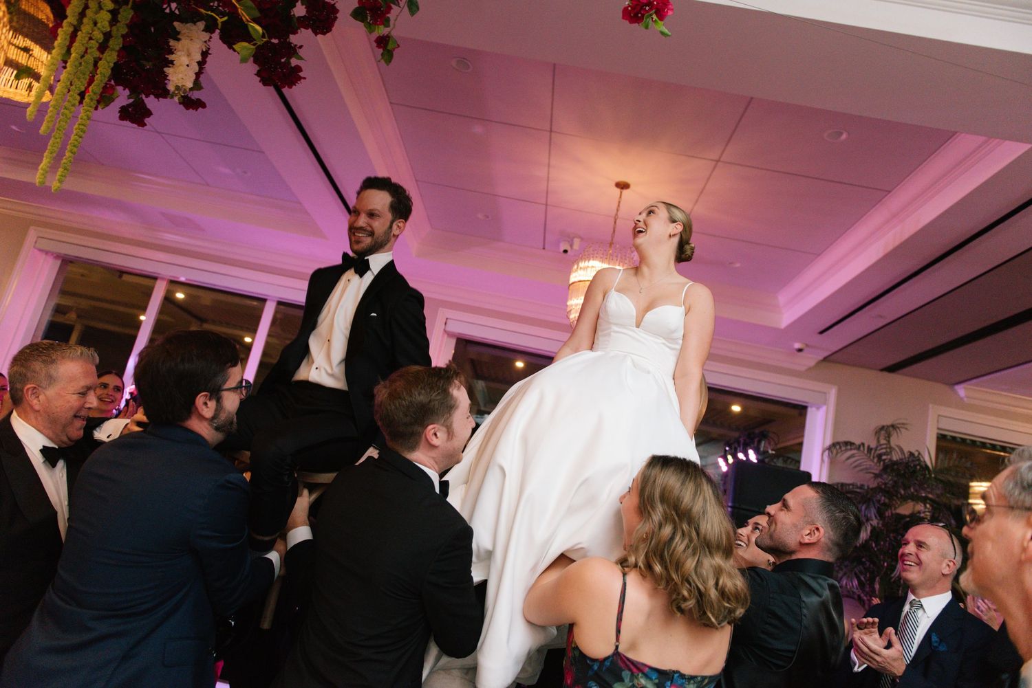 Wedding reception dance floor illuminated with pink uplighting and guests celebrating.