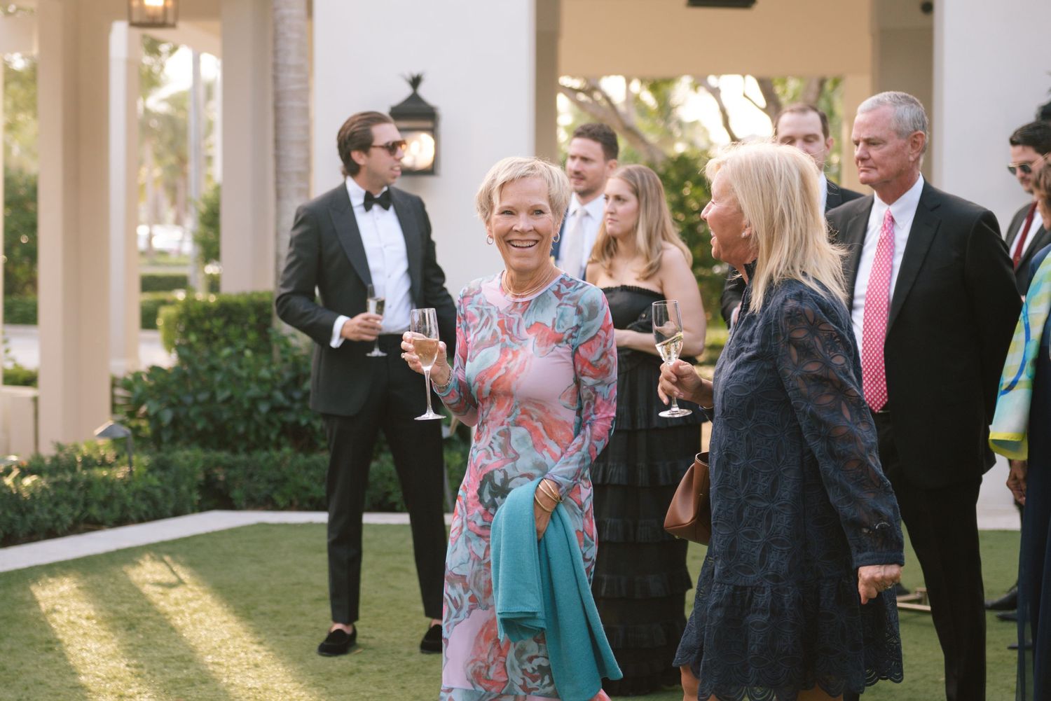 Wedding guests mingling and taking photos on an elegant columned patio at sunset.