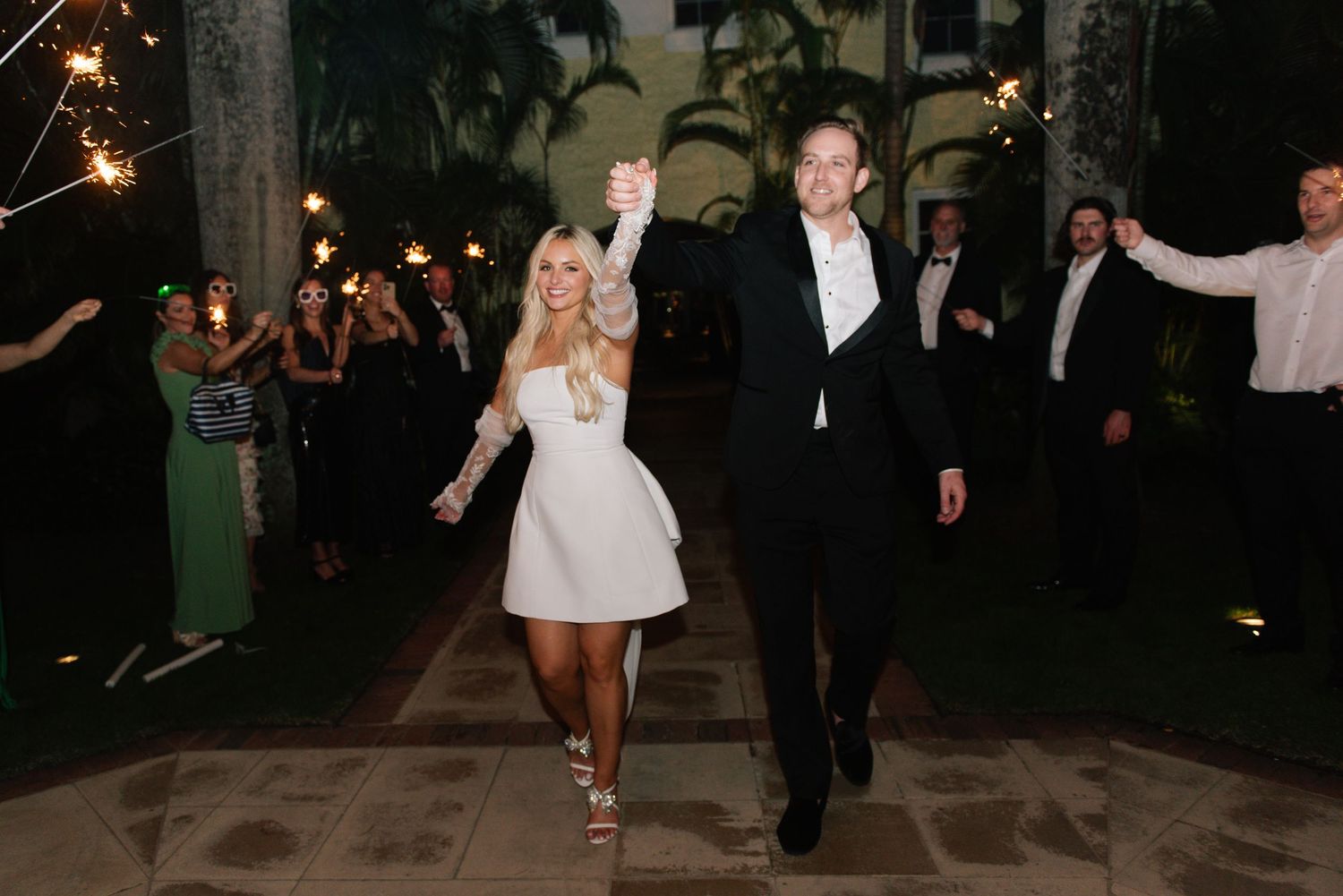 Wedding guests hold sparklers during an evening celebration outdoors.