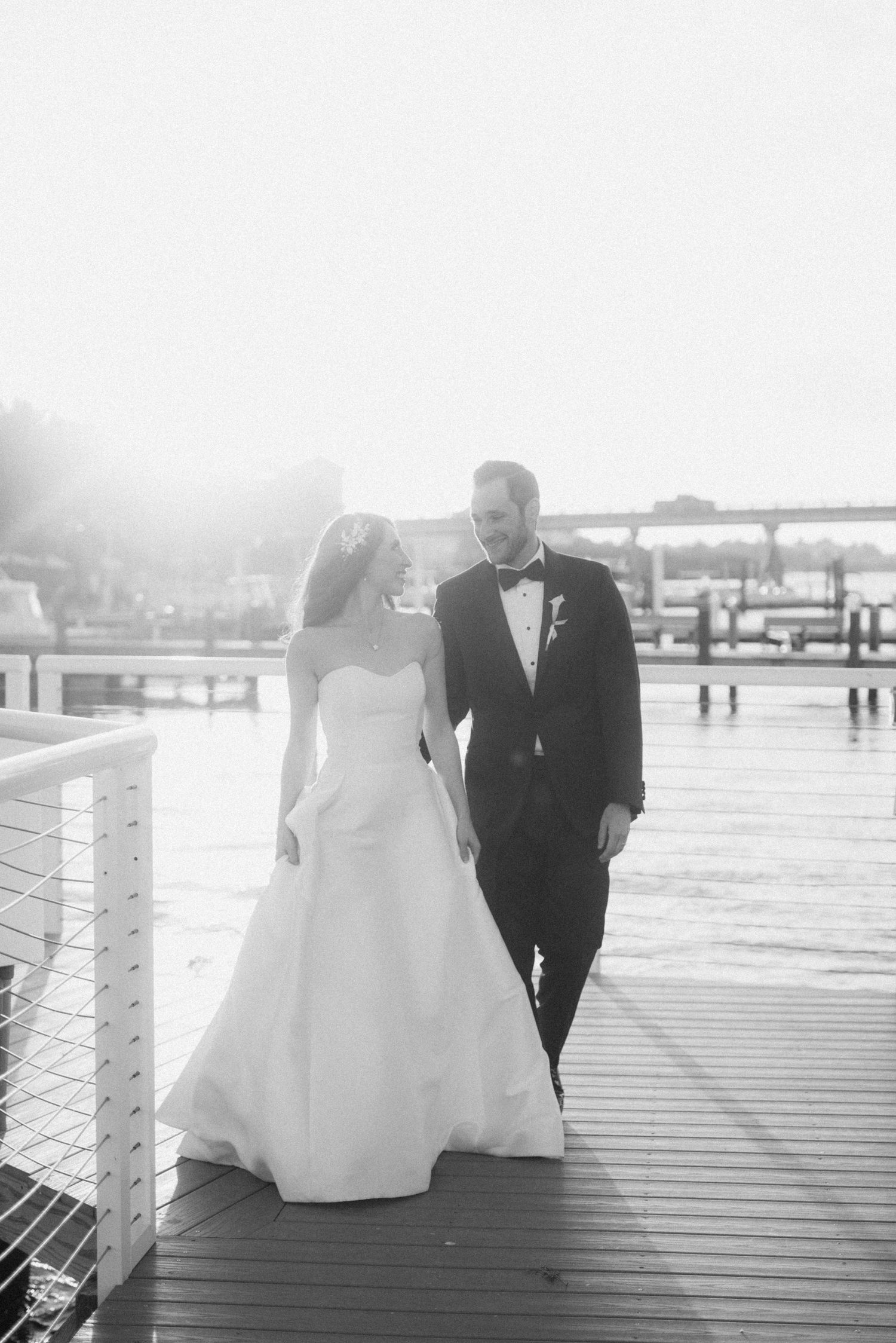 Romantic wedding couple poses on a wooden boardwalk near the water in black and white.