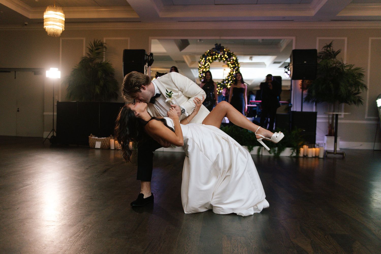 A couple shares a playful dance moment in a dimly lit ballroom with decorative lighting.