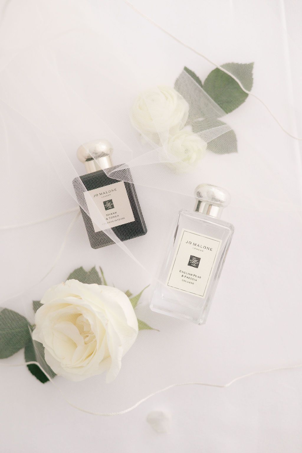 Elegant perfume bottles and white roses arranged on light background for luxury beauty product photography.