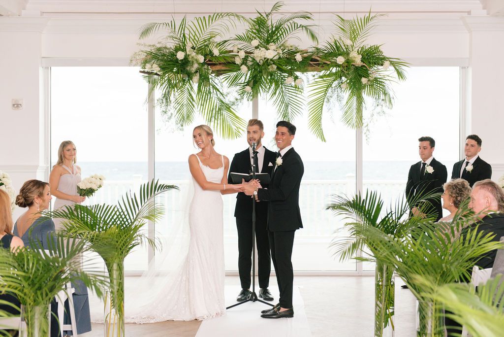 Modern white wedding venue with tropical palm decor and natural lighting.