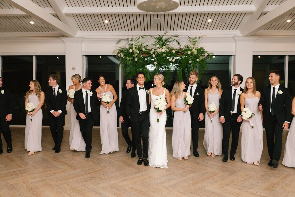 Wedding party poses in formal line inside venue with elegant lighting and decor.