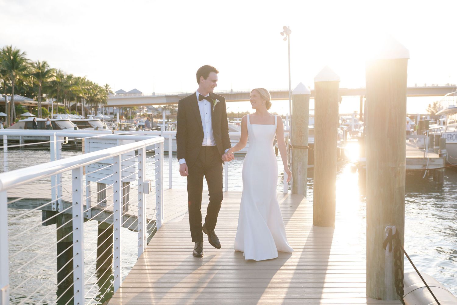 Newlyweds walking along a marina boardwalk at golden hour.