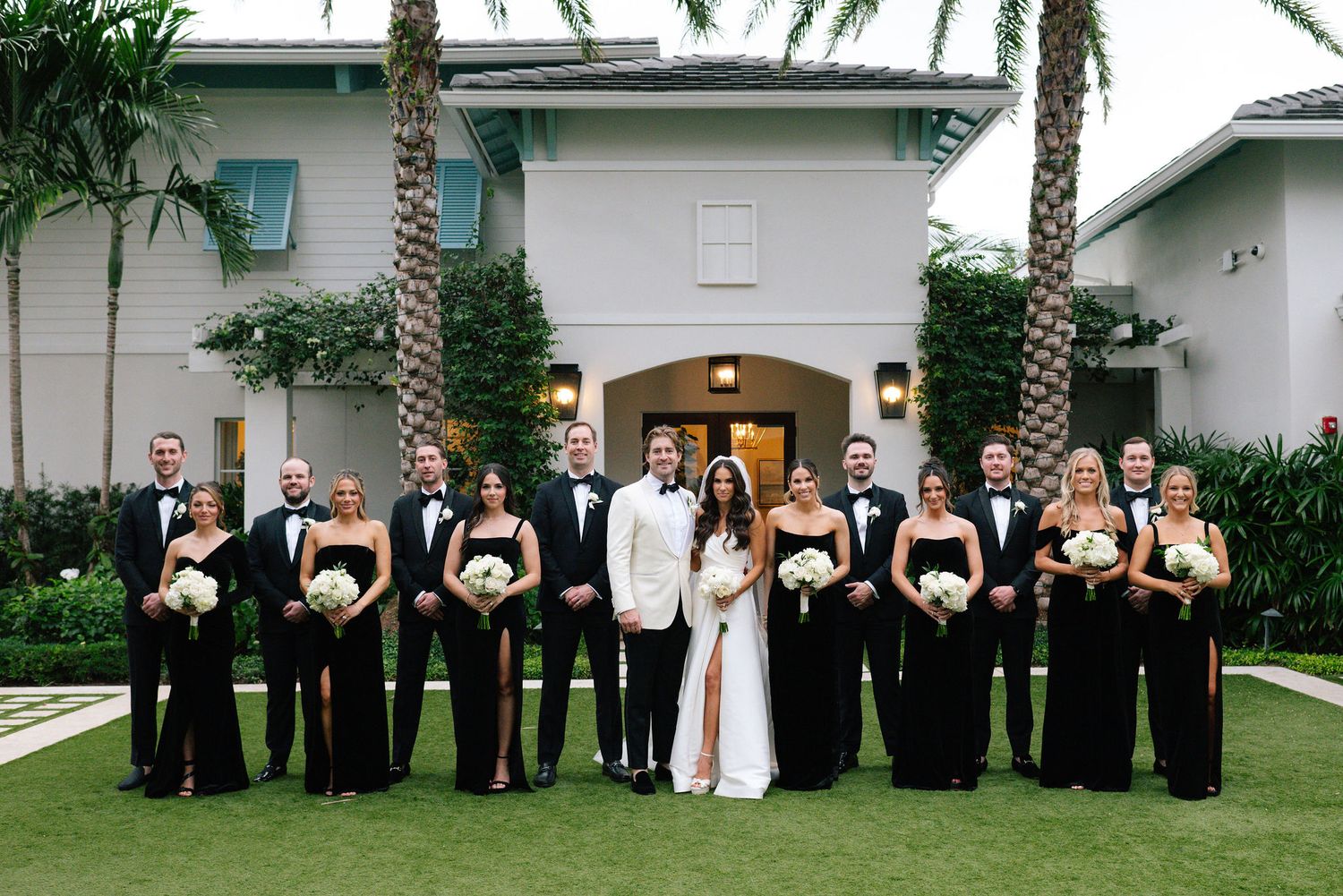 Wedding party members posing for formal group photos on a lawn with white bouquets.