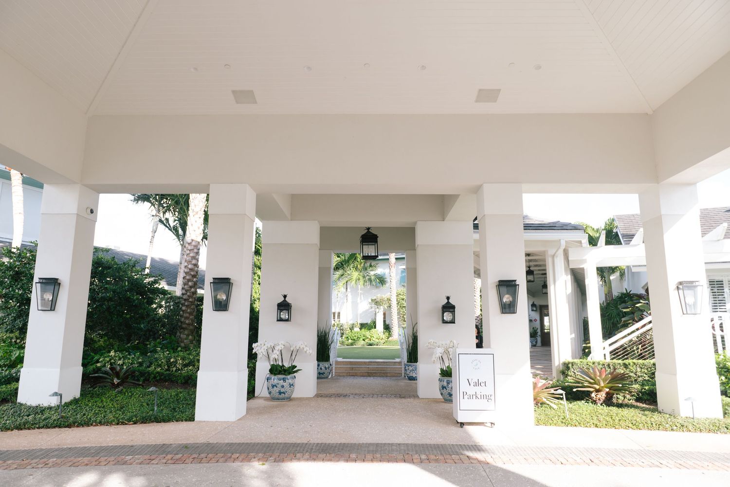 White columned walkway with hanging lanterns and tropical landscaping at luxury venue.