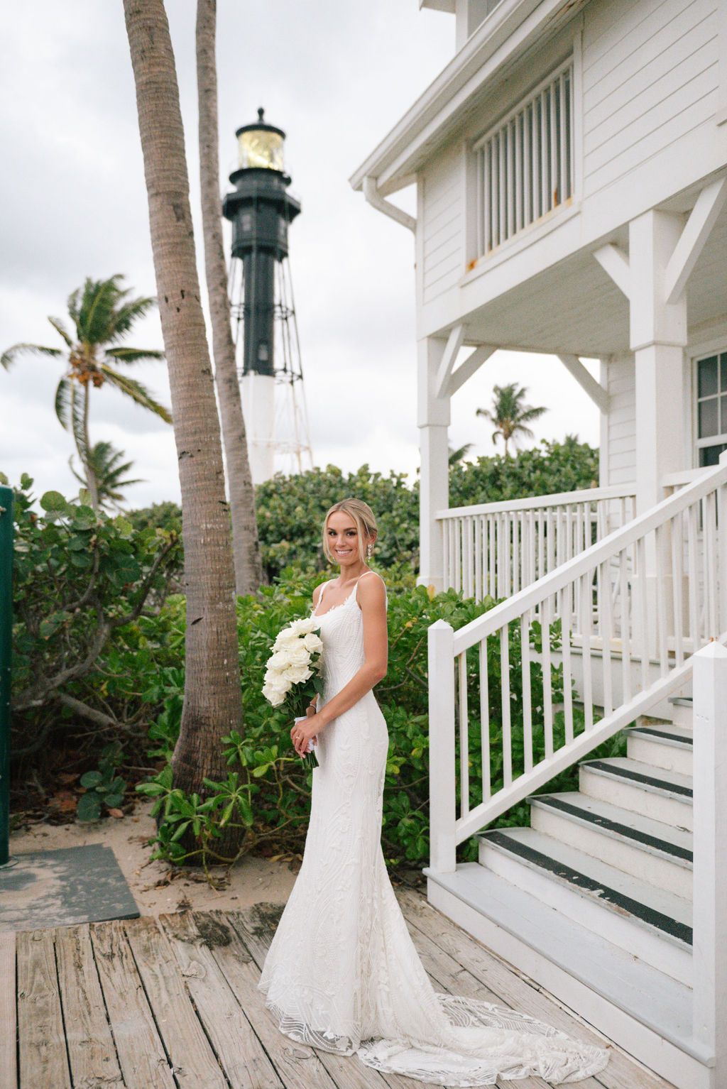 White wedding dress with long train photographed on coastal house deck with palm trees.