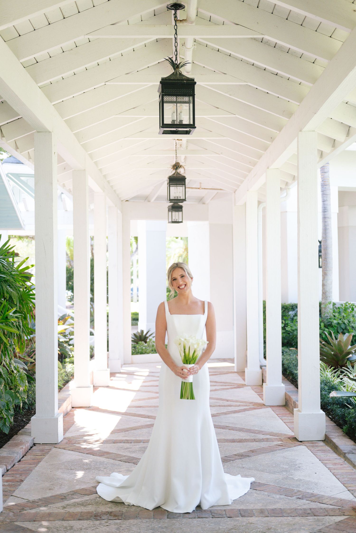 Elegant white wedding dress photographed in a bright columned walkway with hanging lanterns.