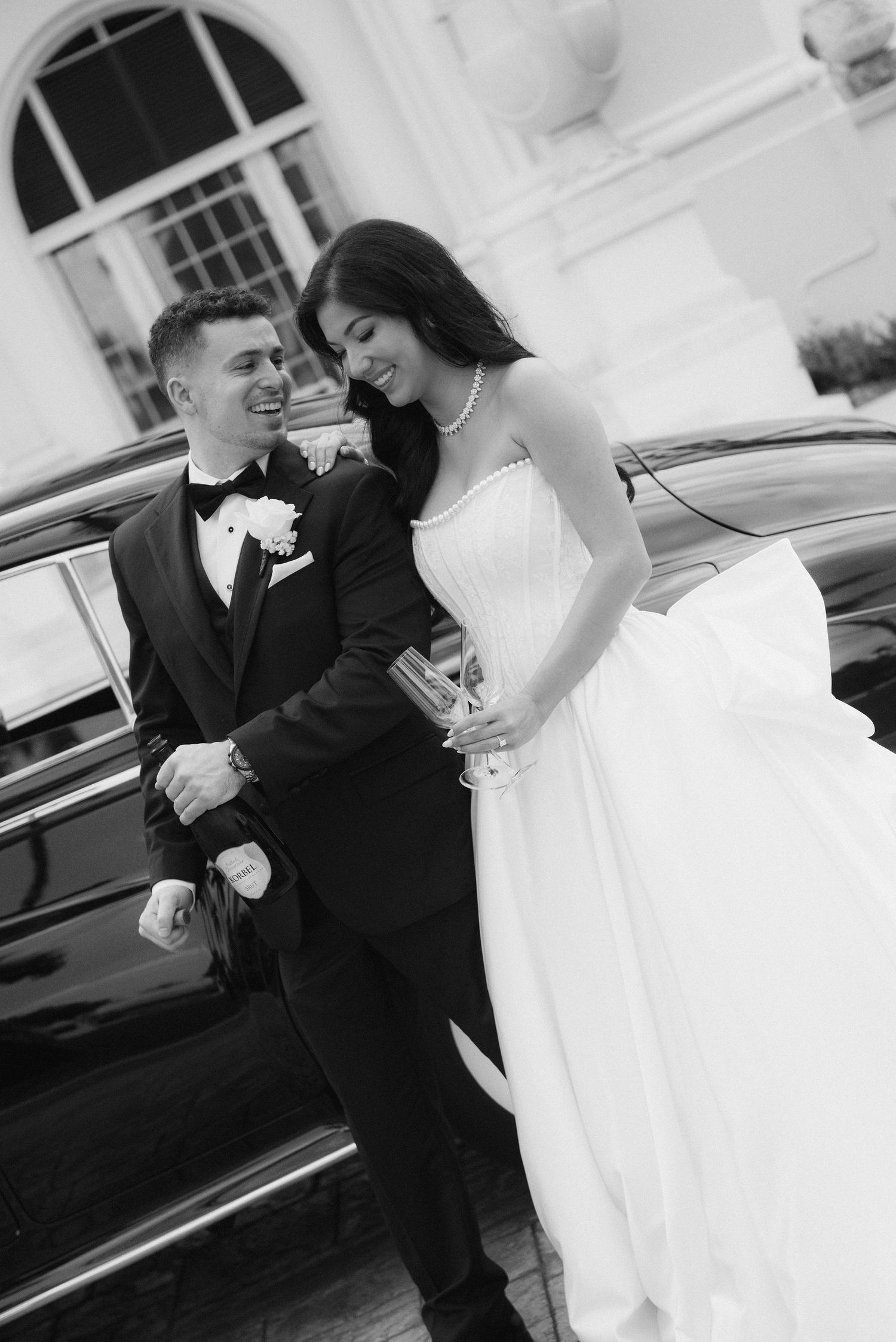 An intimate black and white wedding moment captured outside with a vintage car in the background.