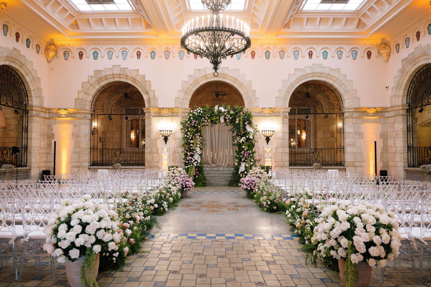Wedding ceremony setup with white chairs and floral arrangements in an elegant indoor venue.