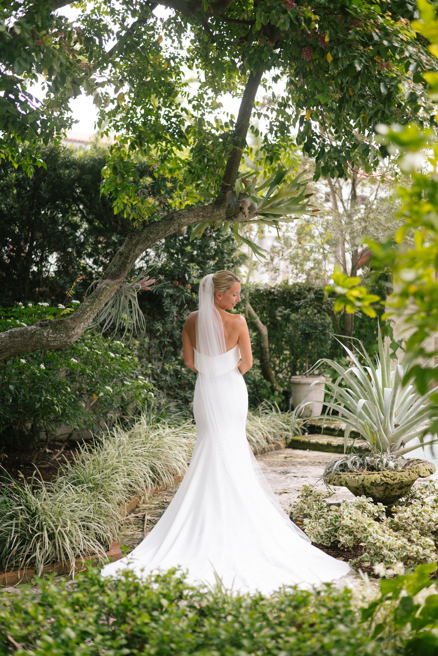 White wedding dress with flowing train photographed in a beautiful garden landscape.