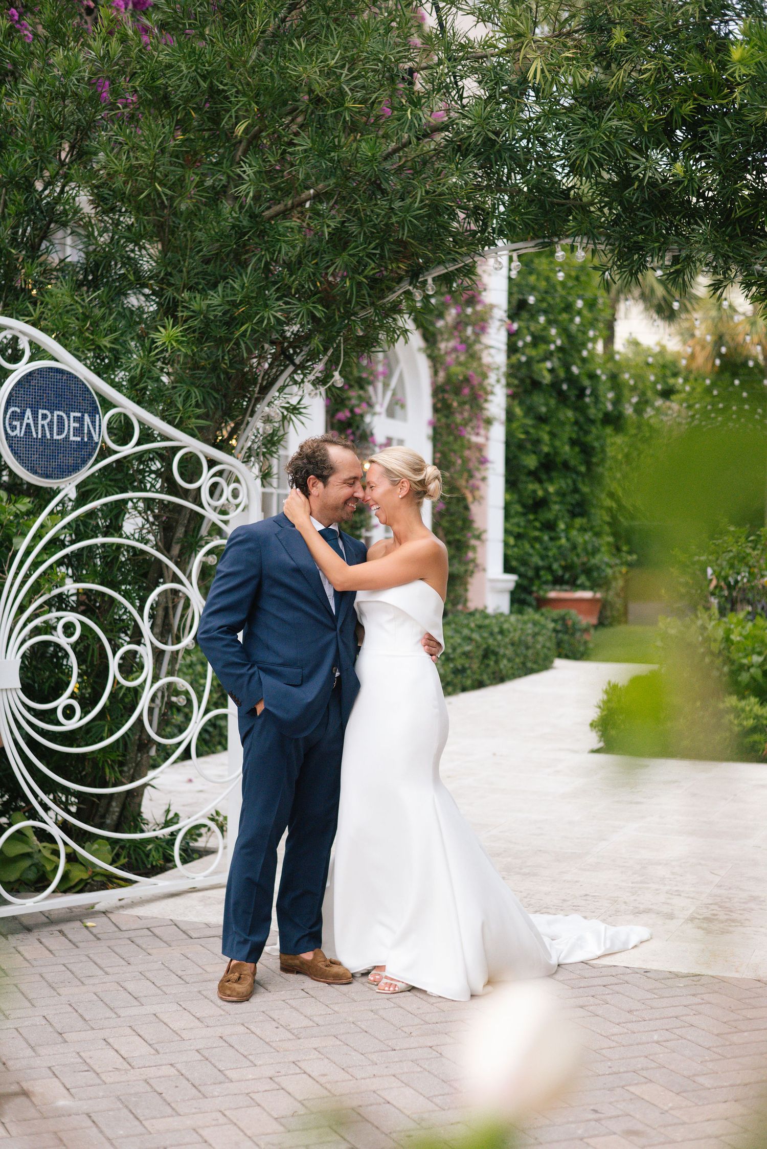 Wedding couple sharing a romantic moment by decorative garden gate surrounded by greenery.