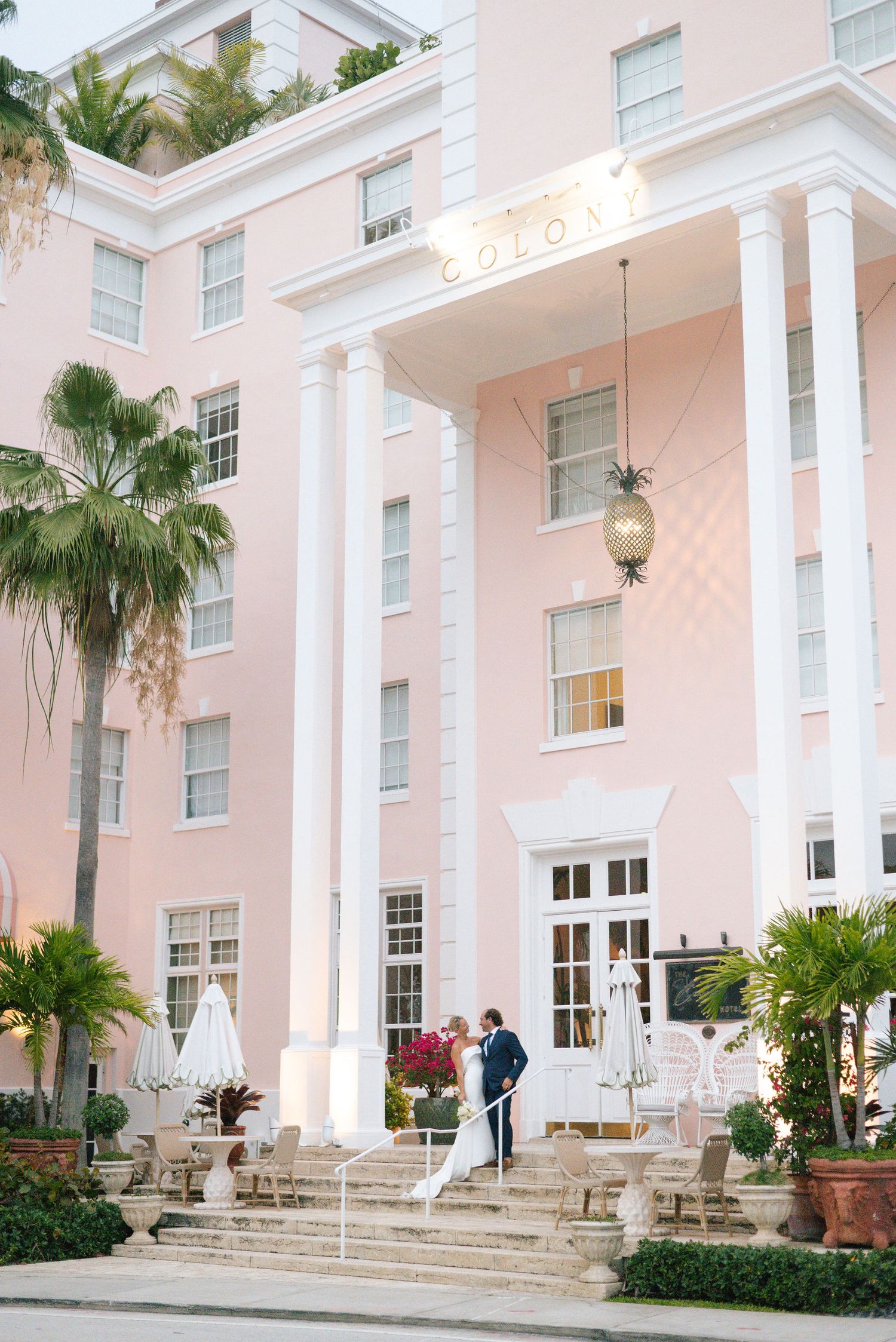 Elegant pink hotel facade with white columns serves as backdrop for wedding photos.