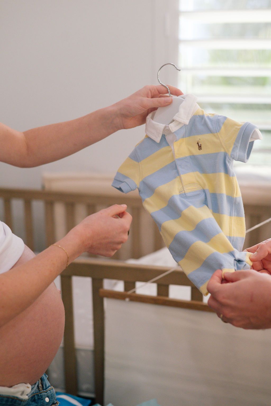 Hands holding and examining a yellow and blue striped baby outfit.