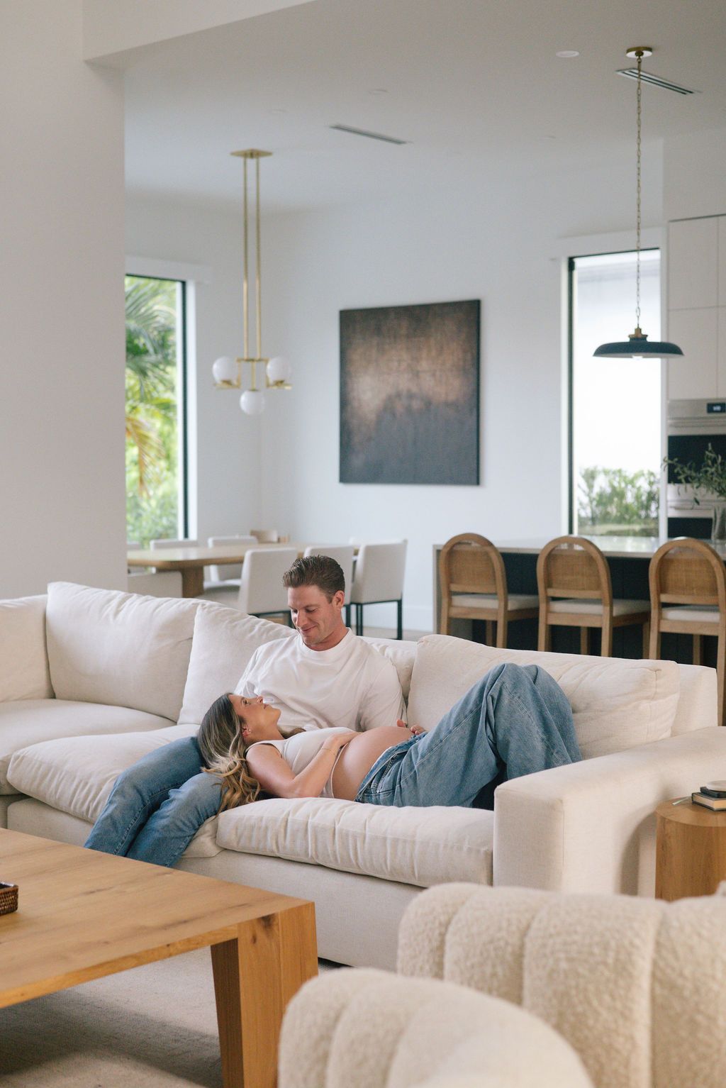 Modern living room interior with white sofa, wooden furniture and large windows letting in natural light.