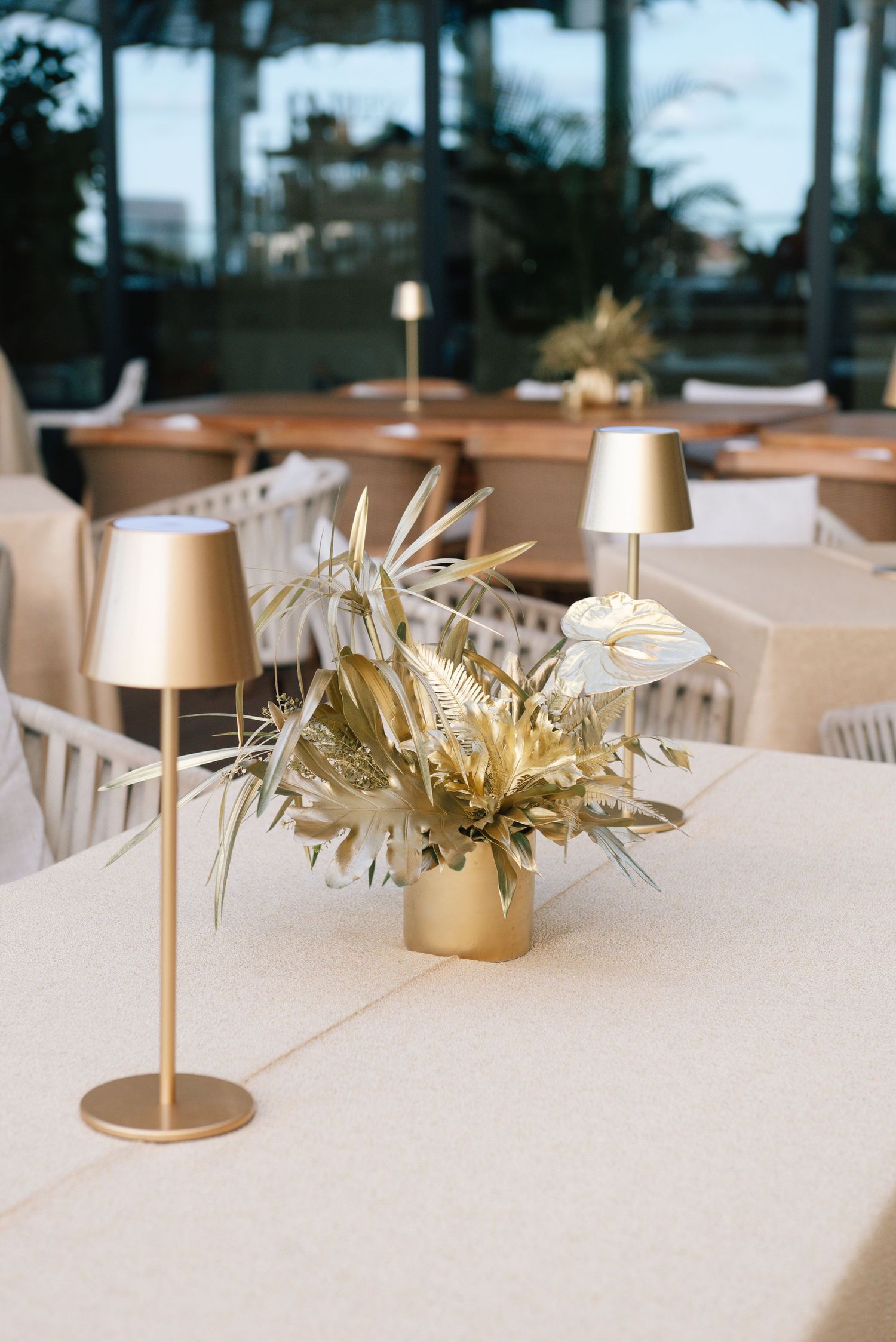 Elegant table settings with gold candle holders and dried palm fronds as centerpieces.