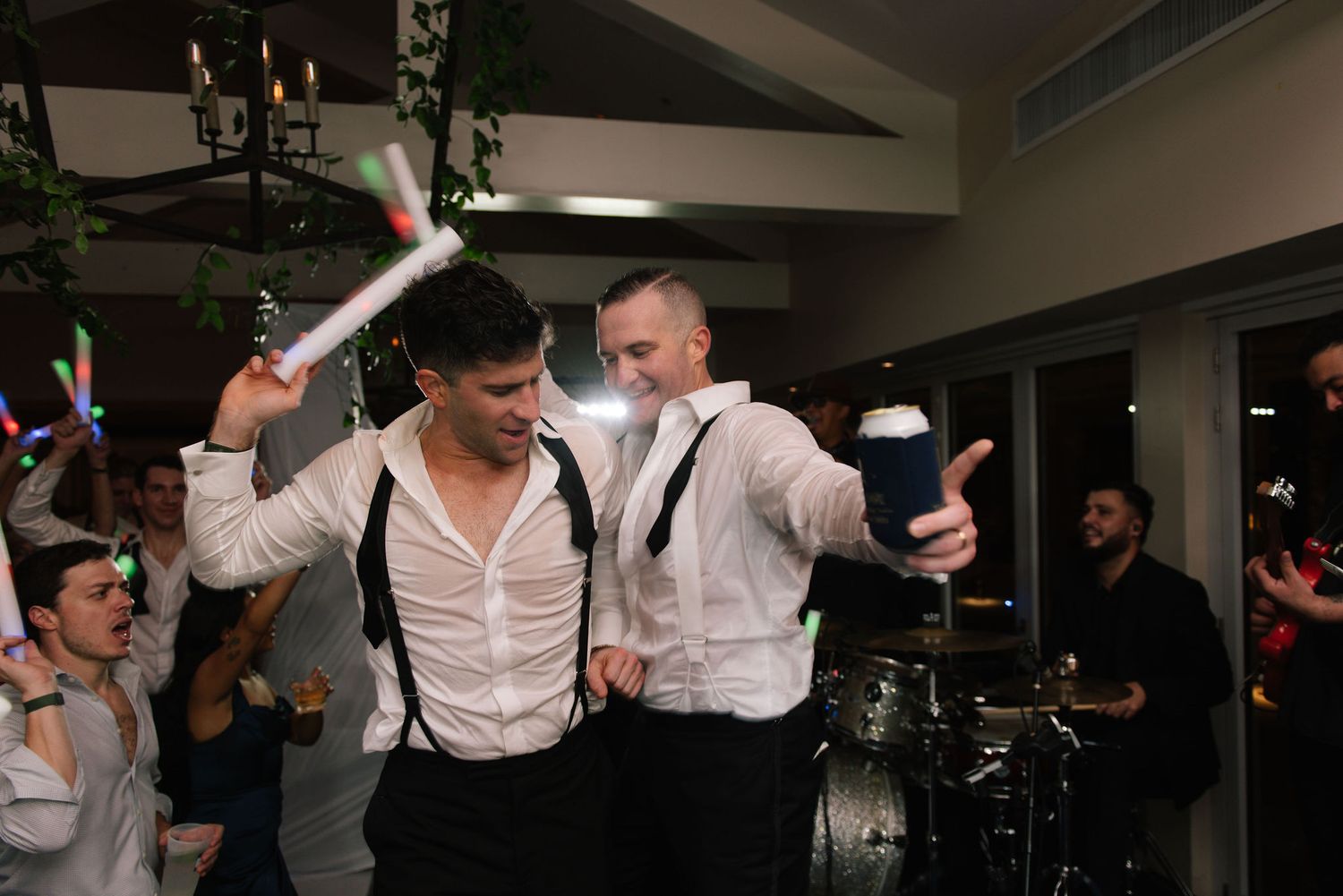 Wedding reception celebration with guests dancing and celebrating in a dimly lit venue.